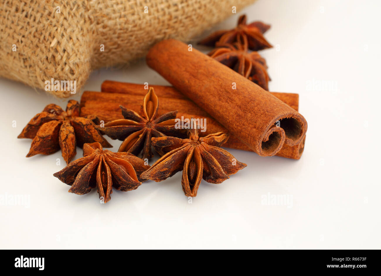 Cinnamon sticks and star aniseed on white reflective background with hessian bag. Selective focus. Macro. Stock Photo