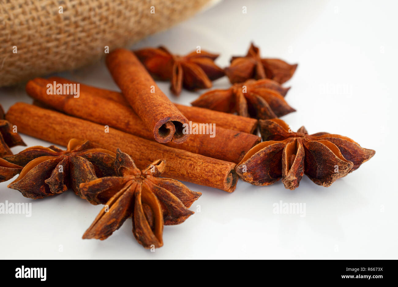 Cinnamon sticks and star aniseed on white reflective background with hessian bag. Selective focus. Macro. Stock Photo
