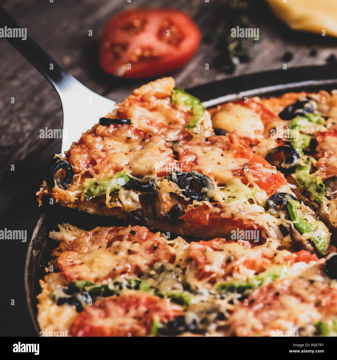 Take piece of pizza with kitchen scapula. Fresh pizza from oven on old wooden table. Square format, matte effect Stock Photo