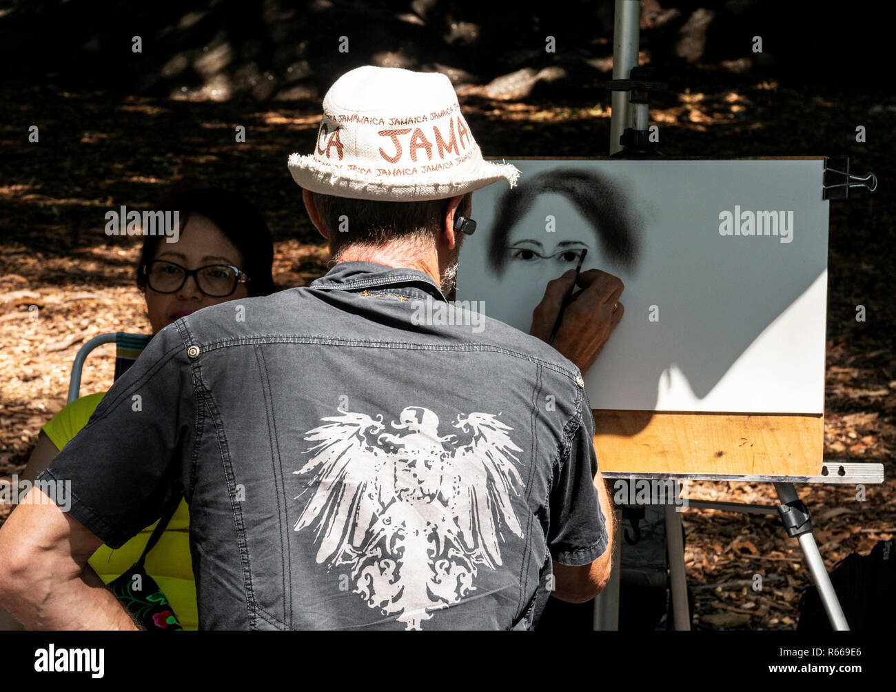 New York City, USA - 15 August 2018: An artist wearing a Jamaica hat is sketching a picture of a women in Central Park NYC. Stock Photo