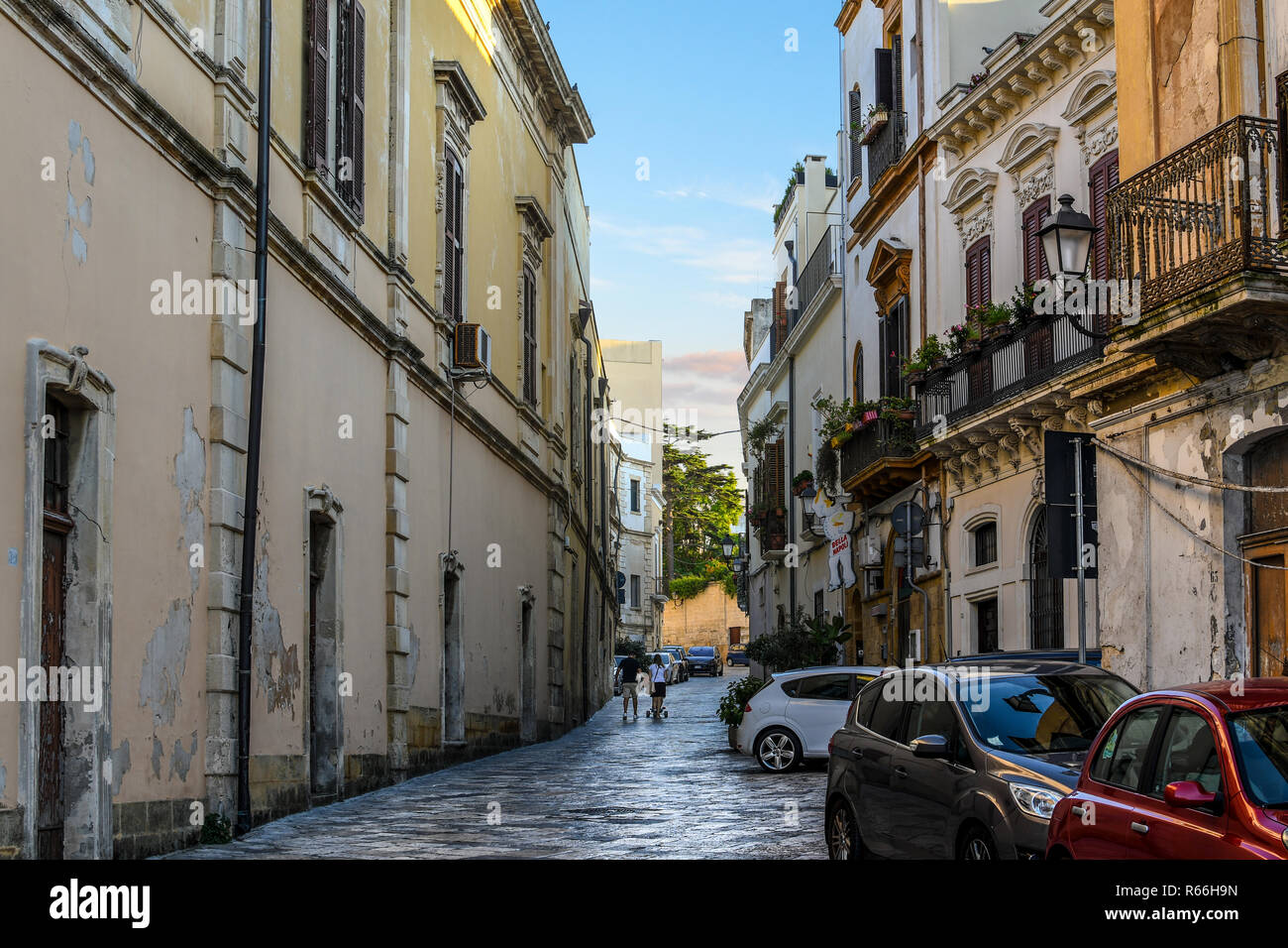 A young couple push a baby stroller down a narrow, dark alley past restaurants and apartments in the historic center of Brindisi, Italy Stock Photo