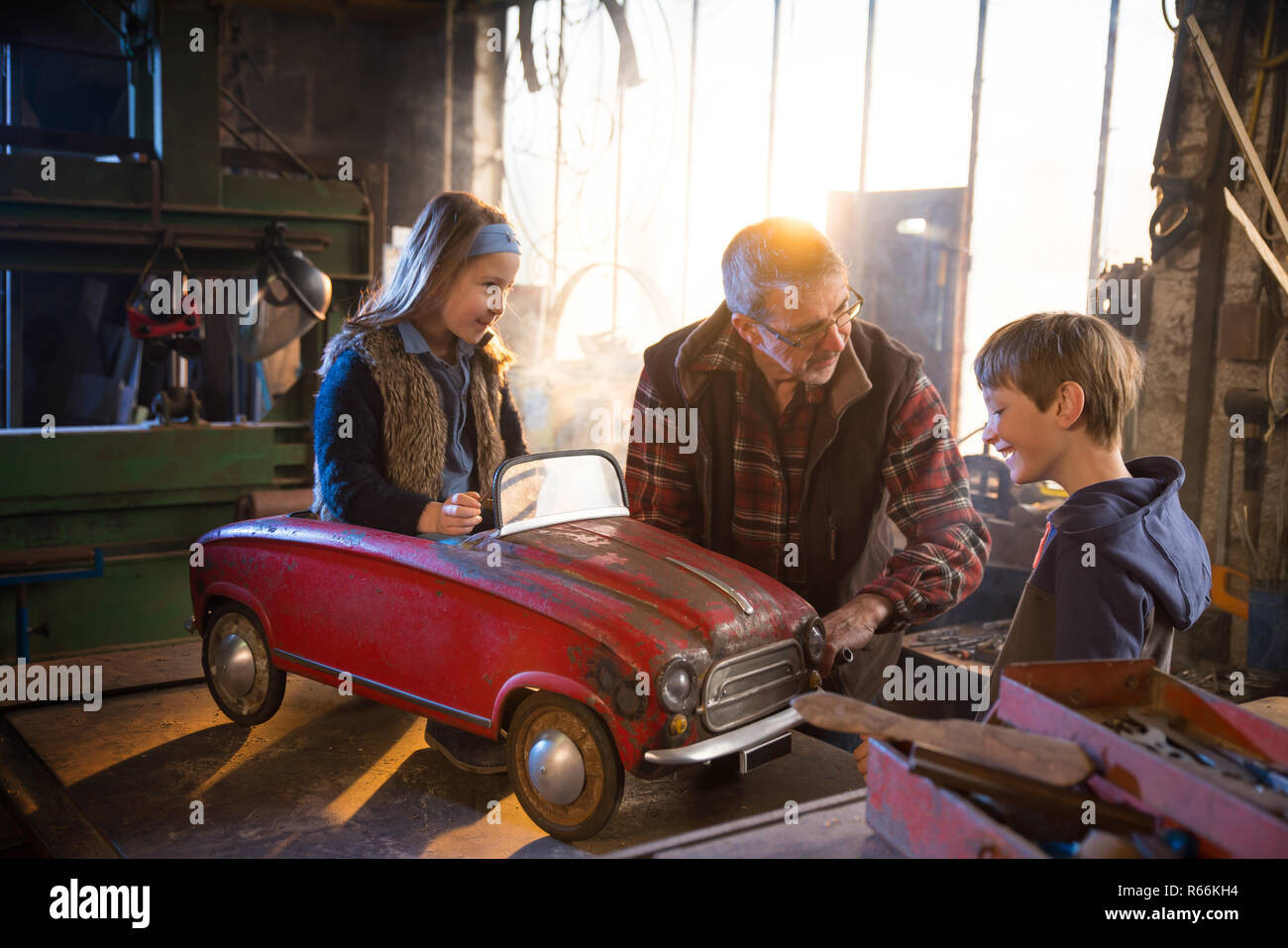 Father and his young childs at workshop, restoring a pedal car Stock Photo