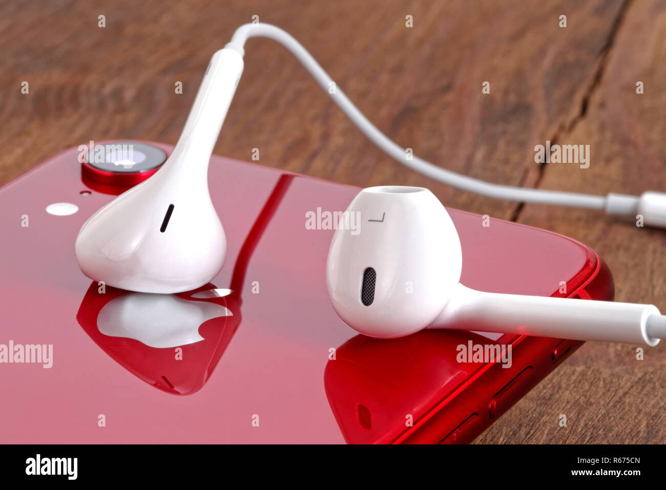 Koszalin, Poland – December 04, 2018: Red iPhone XR on a wooden table with white earphones. The iPhone XR is smart phone with multi touch screen produ Stock Photo