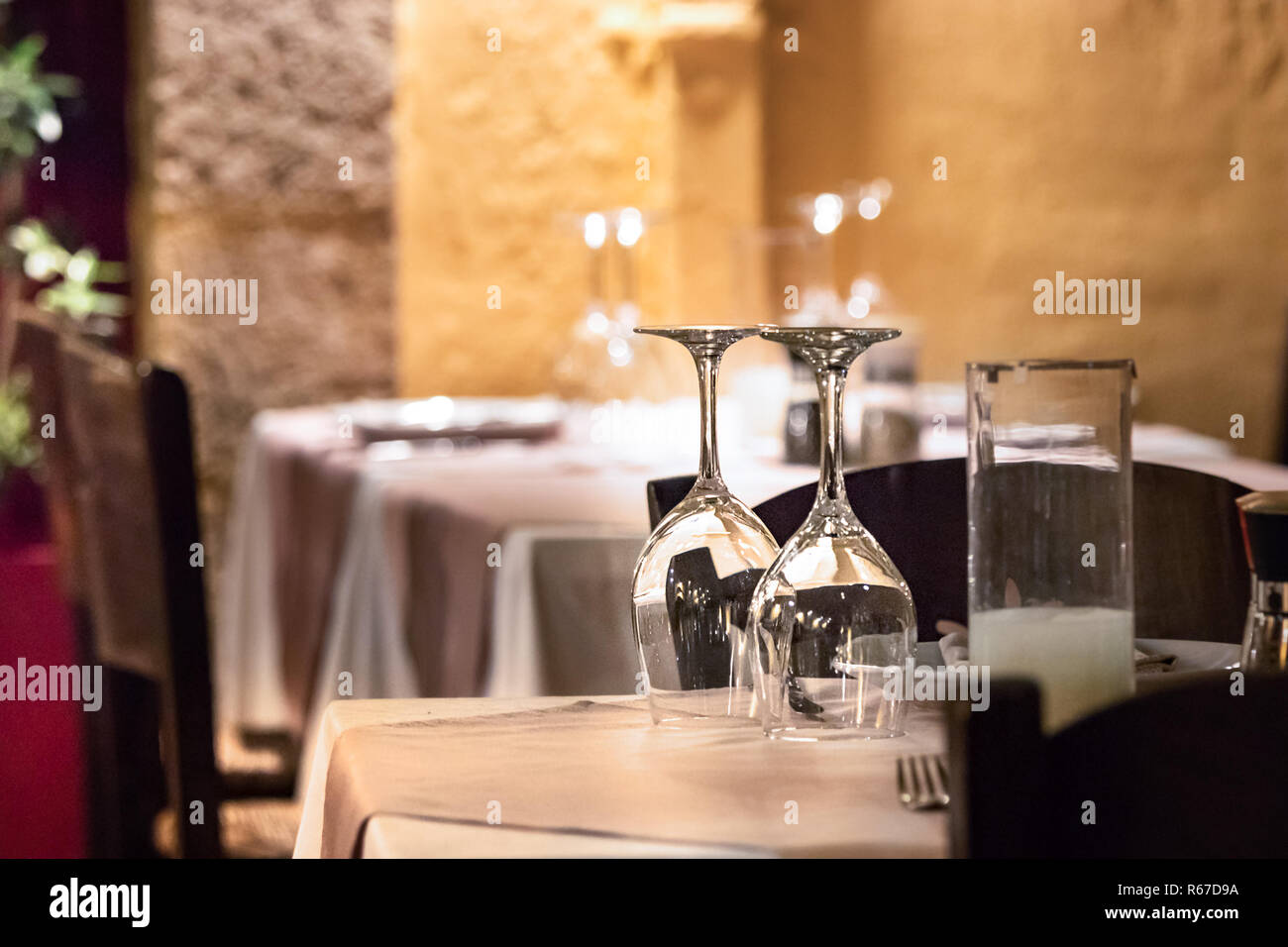 Two wine glasses upside down on a table with shakers, plates and