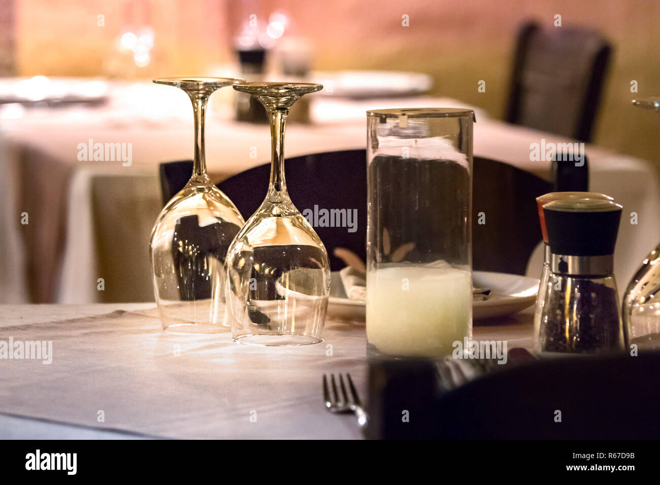 Two wine glasses upside down on a table with shakers, plates and