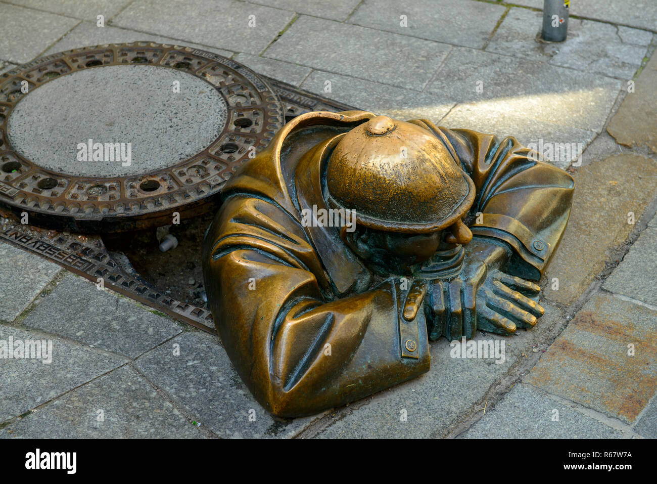 Manhole cover with sculpture Cumil, the spectator by Victor Hulik, 1998, Bratislava, Slovakia Stock Photo