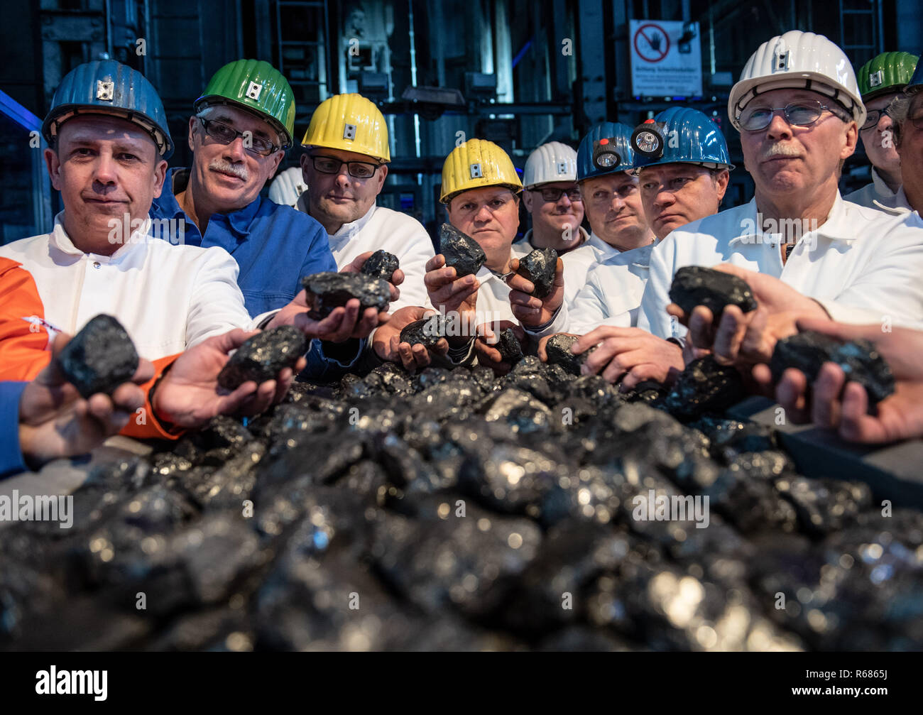 04 December 2018, North Rhine-Westphalia, Ibbenbüren: Miners are standing in front of a winding shaft of Ibbenbüren colliery with pieces of coal from the last wagon to be mined. Subsidised coal mining in Germany will be phased out at the end of 2018. The last colliery, Prosper Haniel, closes on 21.12. in Bottrop. Photo: Bernd Thissen/dpa Stock Photo