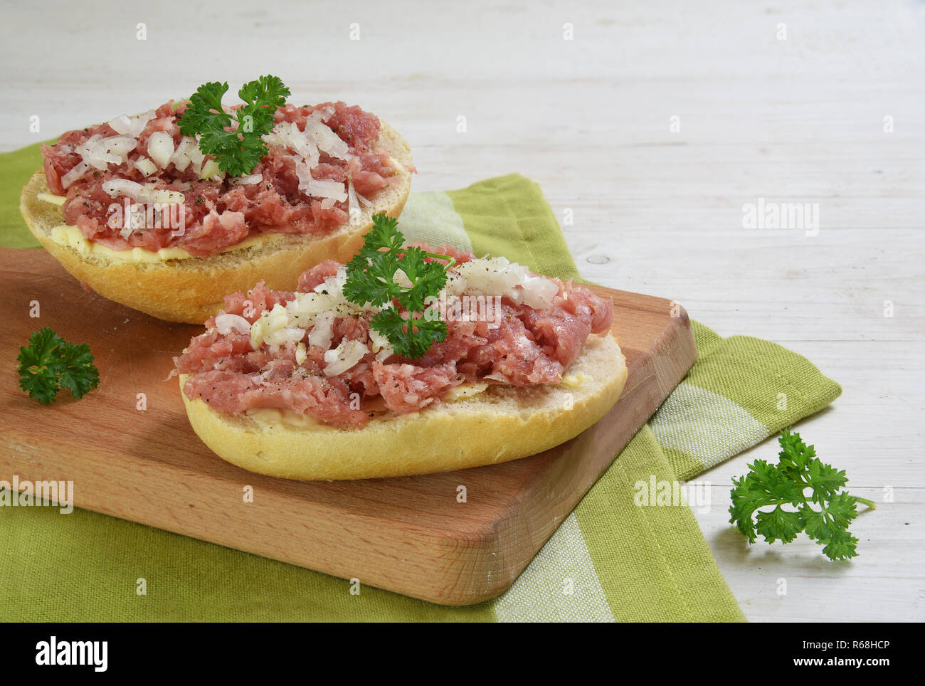 Bread rolls with minced pork sausage, german zwiebelmettwurst with onions and parsley garnish on a breakfast board,  green napkin and white wooden bac Stock Photo