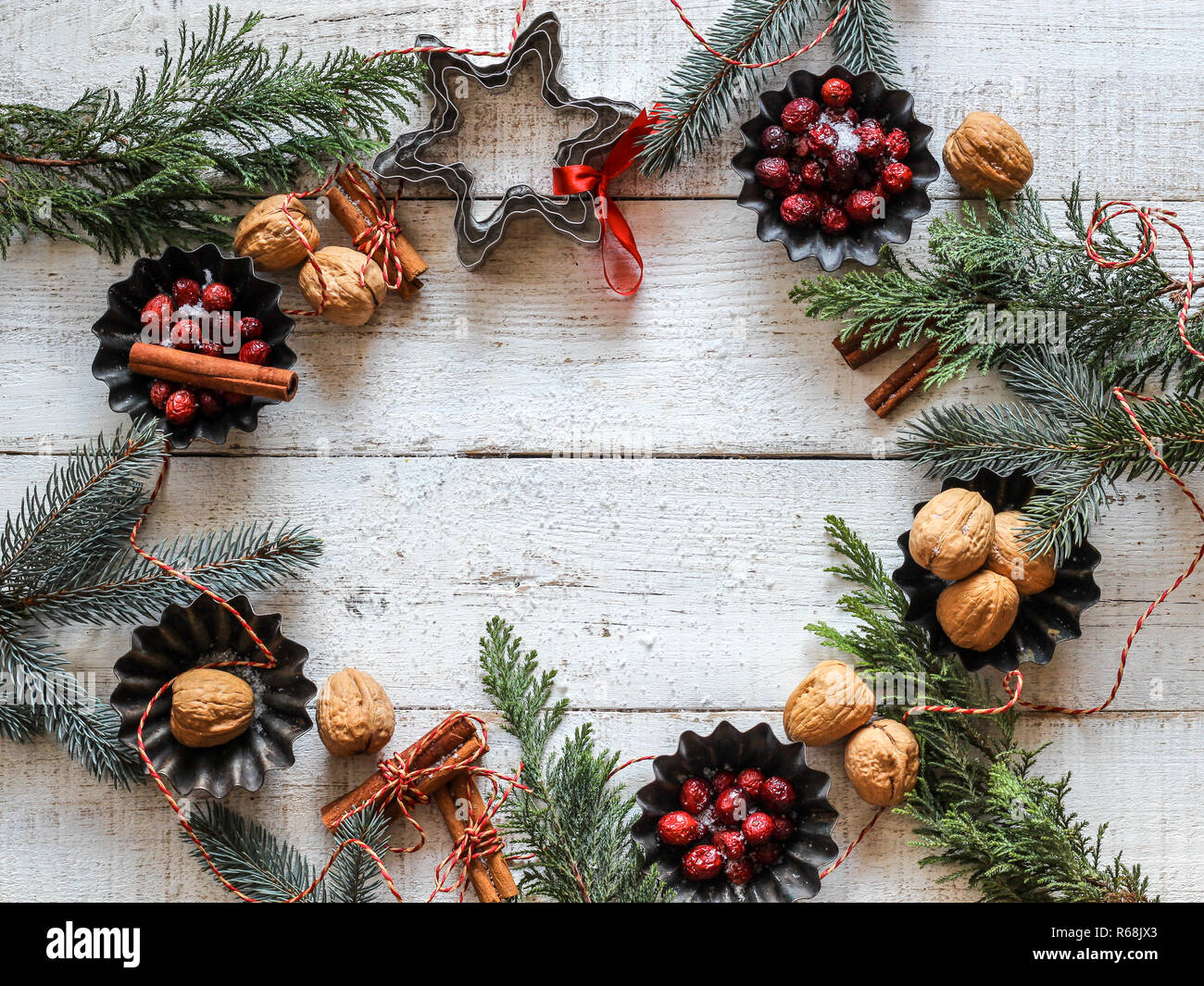 Christmas flat lay in circle form made from evergreens, red berries, nuts and cinnamon sticks on white wooden background. Space for product or text Stock Photo