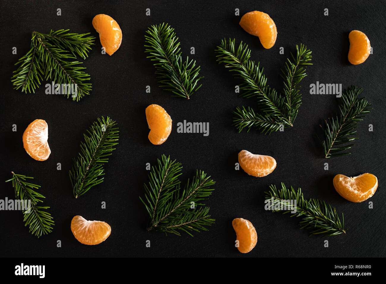 Flat lay pattern of orange mandarin slices and small fir branches on dark textured background. Stock Photo