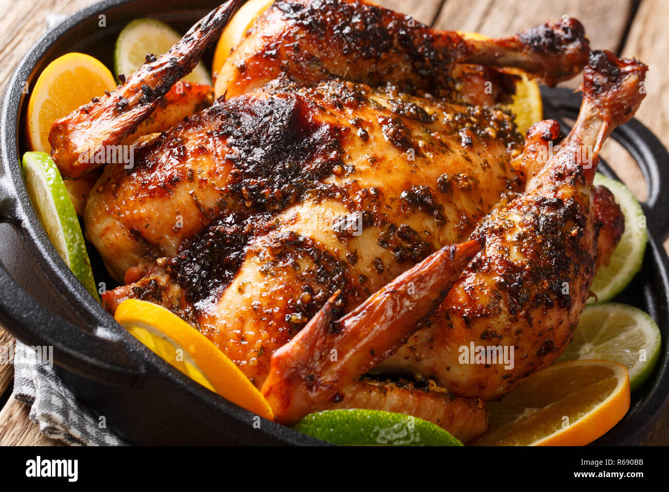 Whole baked Cuban chicken marinated with mojo sauce served with oranges and lime close-up in a frying pan. horizontal Stock Photo