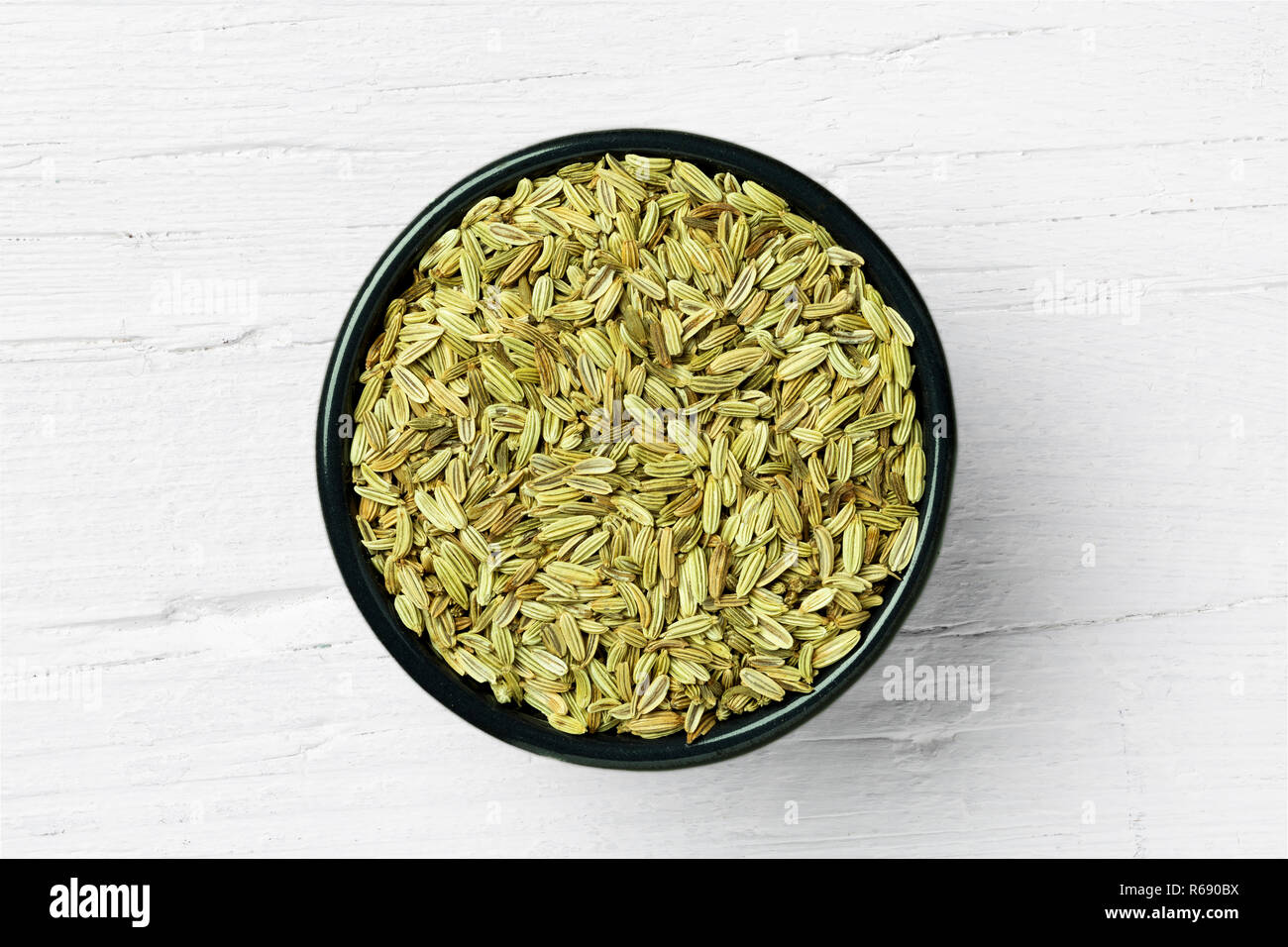 Round cup with fennel seed on white wooden background, view directly from above. Stock Photo