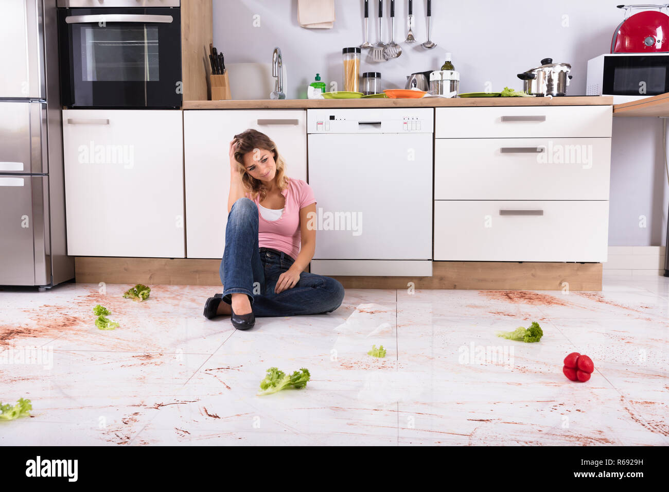 Woman Sitting On Messy Kitchen Floor Stock Photo