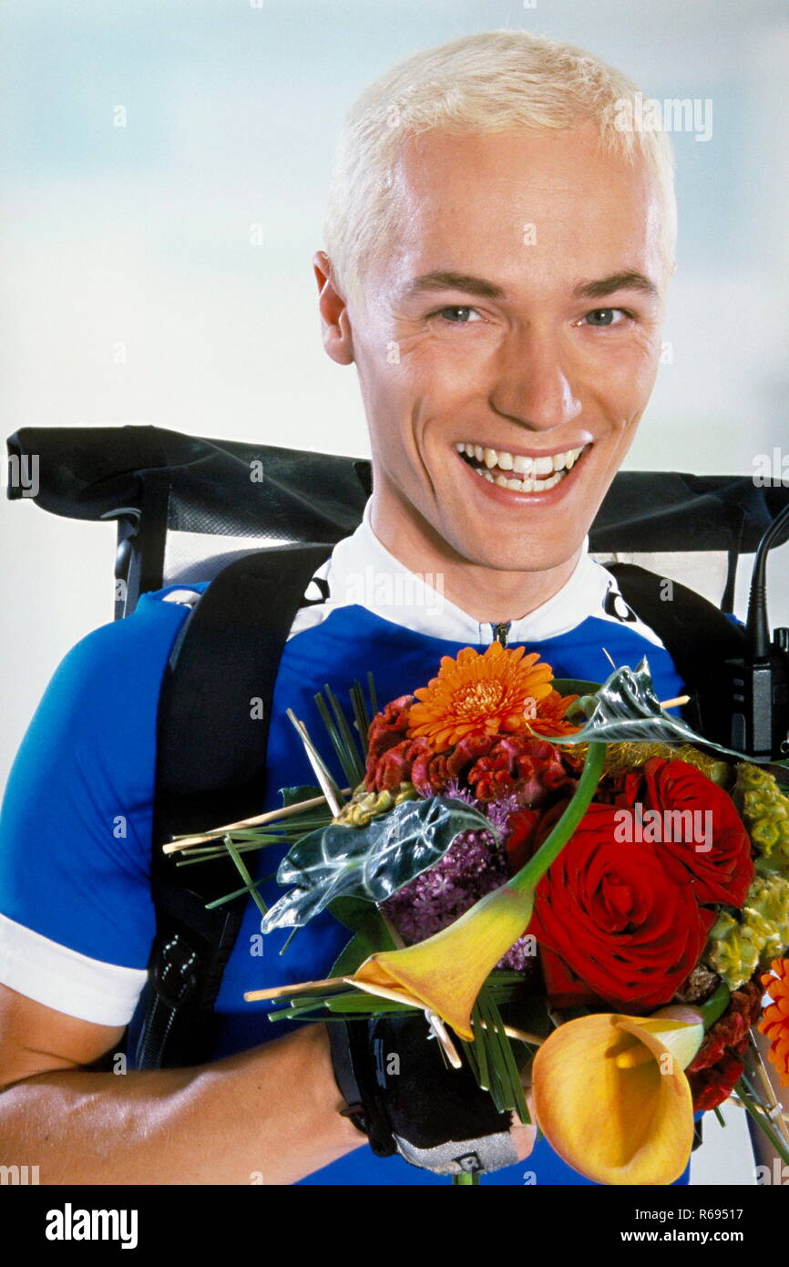 Portrait, Innenraum, laechelnder ca. 30 Jahre alter blonder Fahrradkurier mit einem Blumenstrauss in der Hand Stock Photo