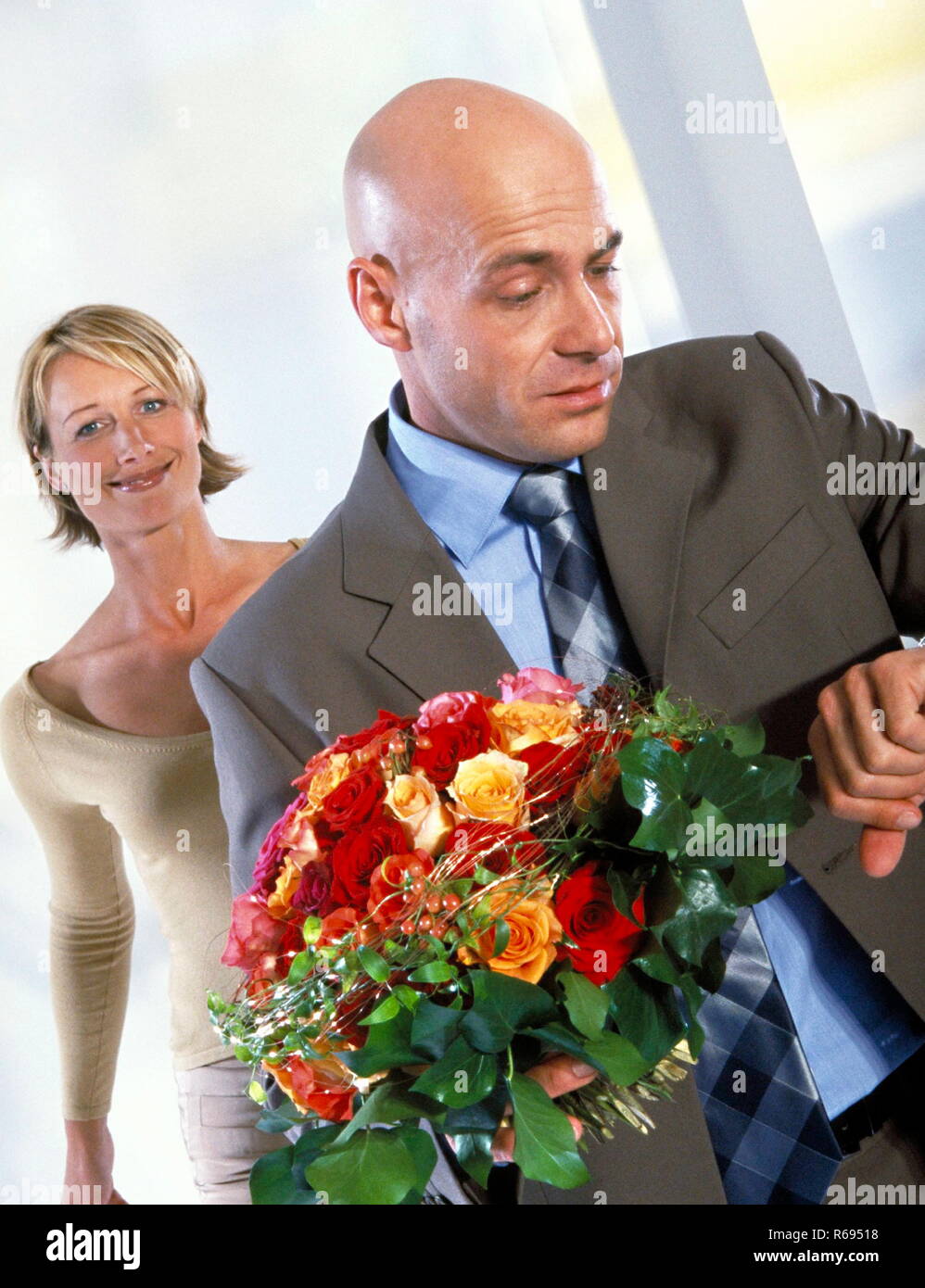 Portrait, Innenraum, blonde Frau und glatzkoepfiger Mann im grauen Anzug mit Strauss Rosen in der Hand Stock Photo