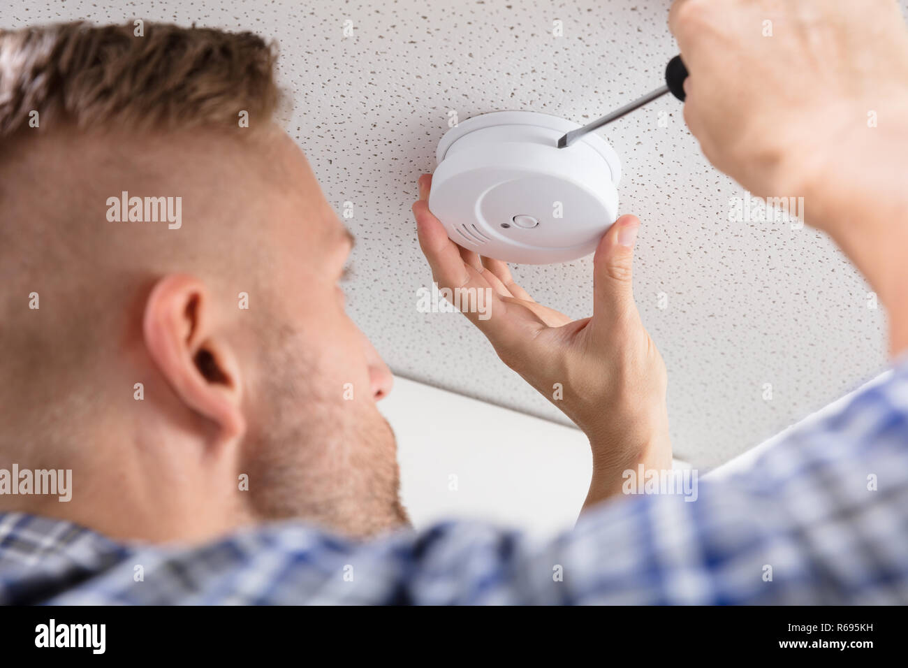 Person's Hand Using Screwdriver To Install Smoke Detector Stock Photo