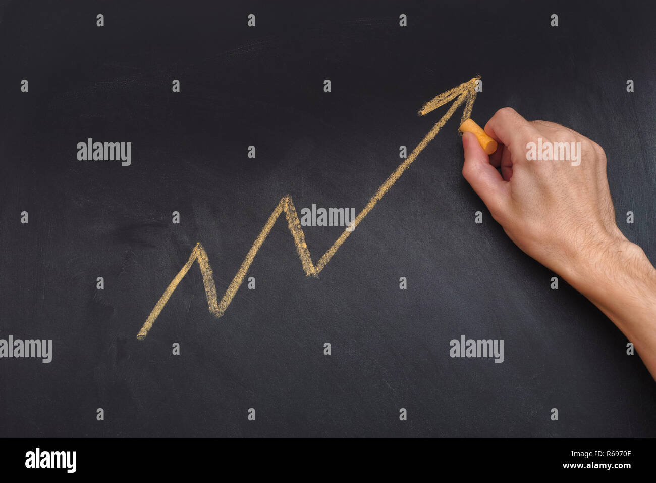 Man drawing yellow arrow showing upward trend and increasing profits on blackboard. Close up. Stock Photo