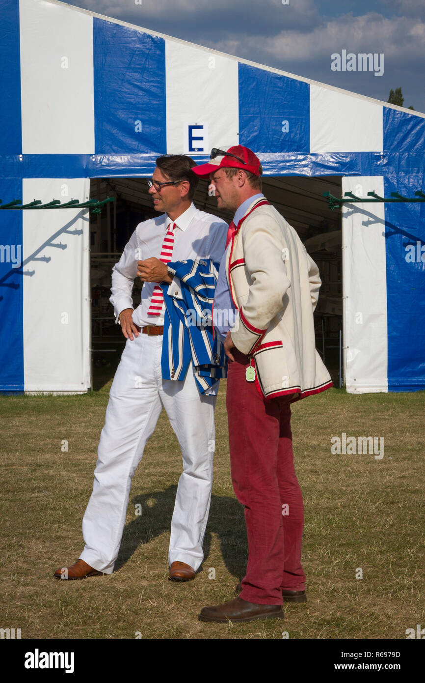 Two men in rowing blazers stand in front of the Boat Tents at Henley