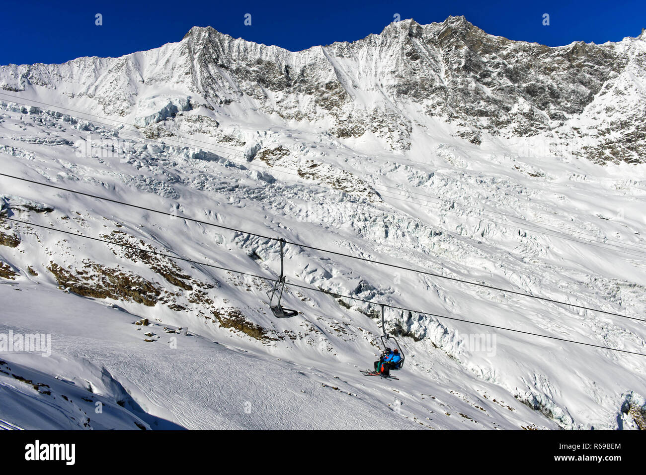 Skiers On A Chairlift Against The Fee Glacier And The Mischabel Massif, Saas-Fee, Switzerland Stock Photo