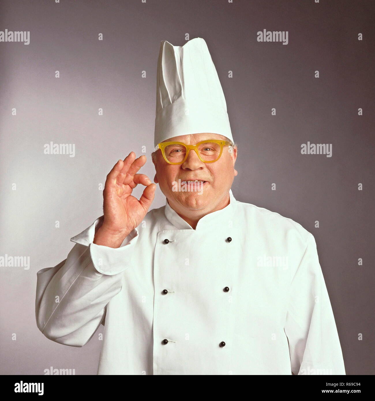 Portrait, Halbfigur, Chefkoch in Arbeitskleidung mit gelber Hornbrille Stock Photo