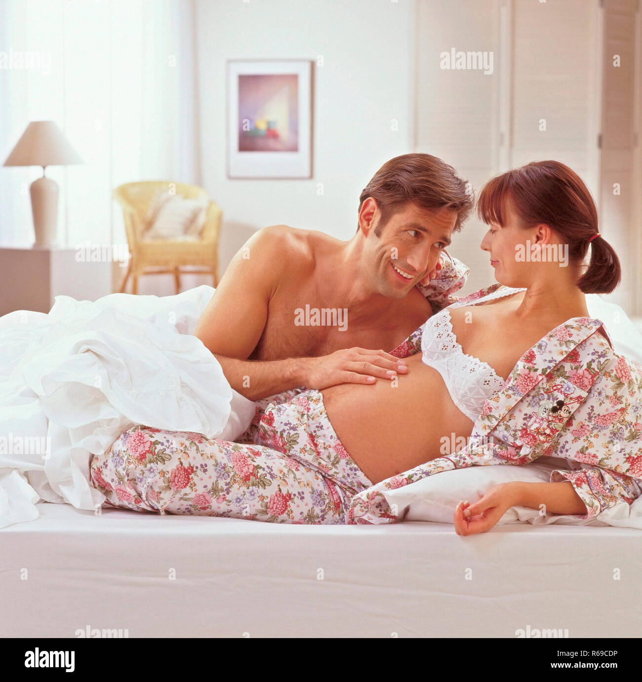 Portrait, Mann liegt mit seiner hochschwangeren Frau auf dem Bett und  beruehrt ihren Bauch Stock Photo - Alamy