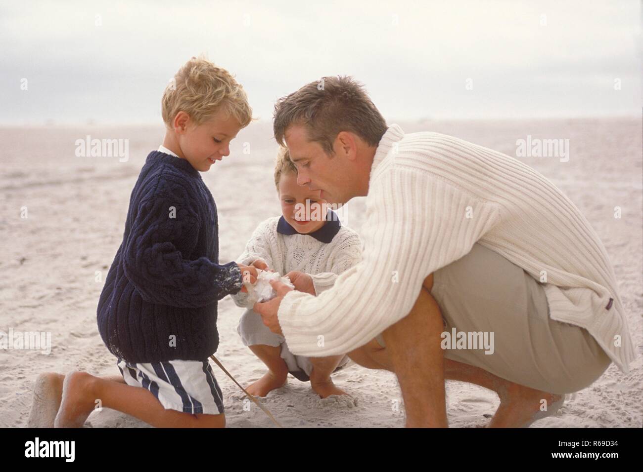 Strandszene, Mann spielt mit seinen beiden 5-7 Jahre alten blonden Soehnen barfuss am Strand Stock Photo