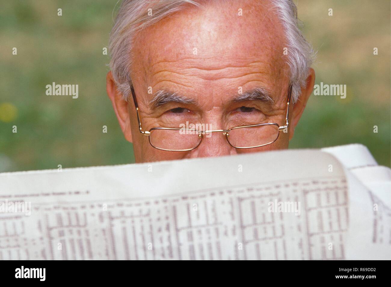 Portrait, Nahaufnahme, grauhaariger Senior, ca. 70 Jahre alt, mit Lesebrille im Garten hinter seiner Zeitung Stock Photo
