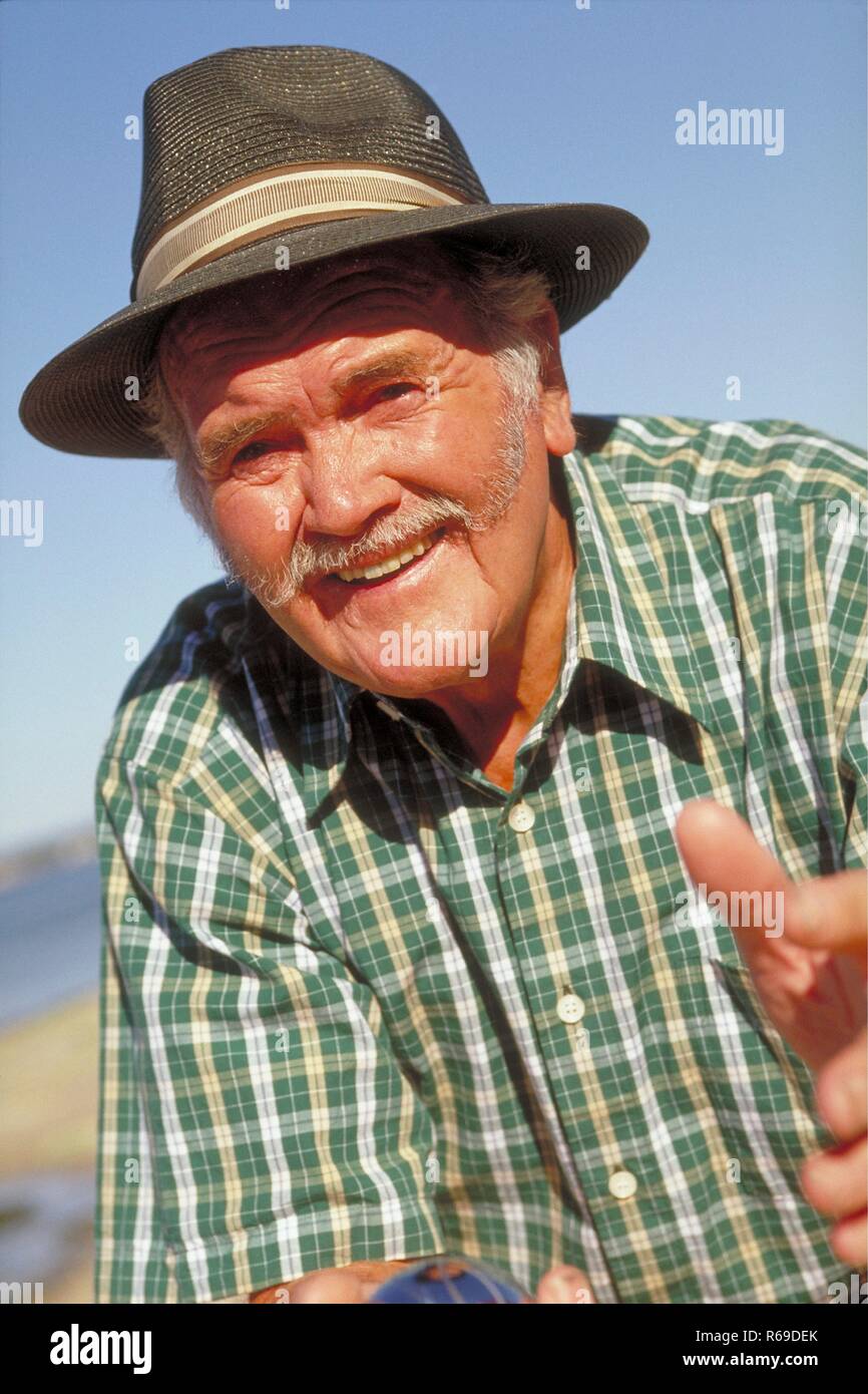 Portrait, Outdoor, Mann mit Oberlippenbart, ca. 65 Jahre alt, bekleidet mit gruen-weiss kariertem Hemd und Hut Stock Photo