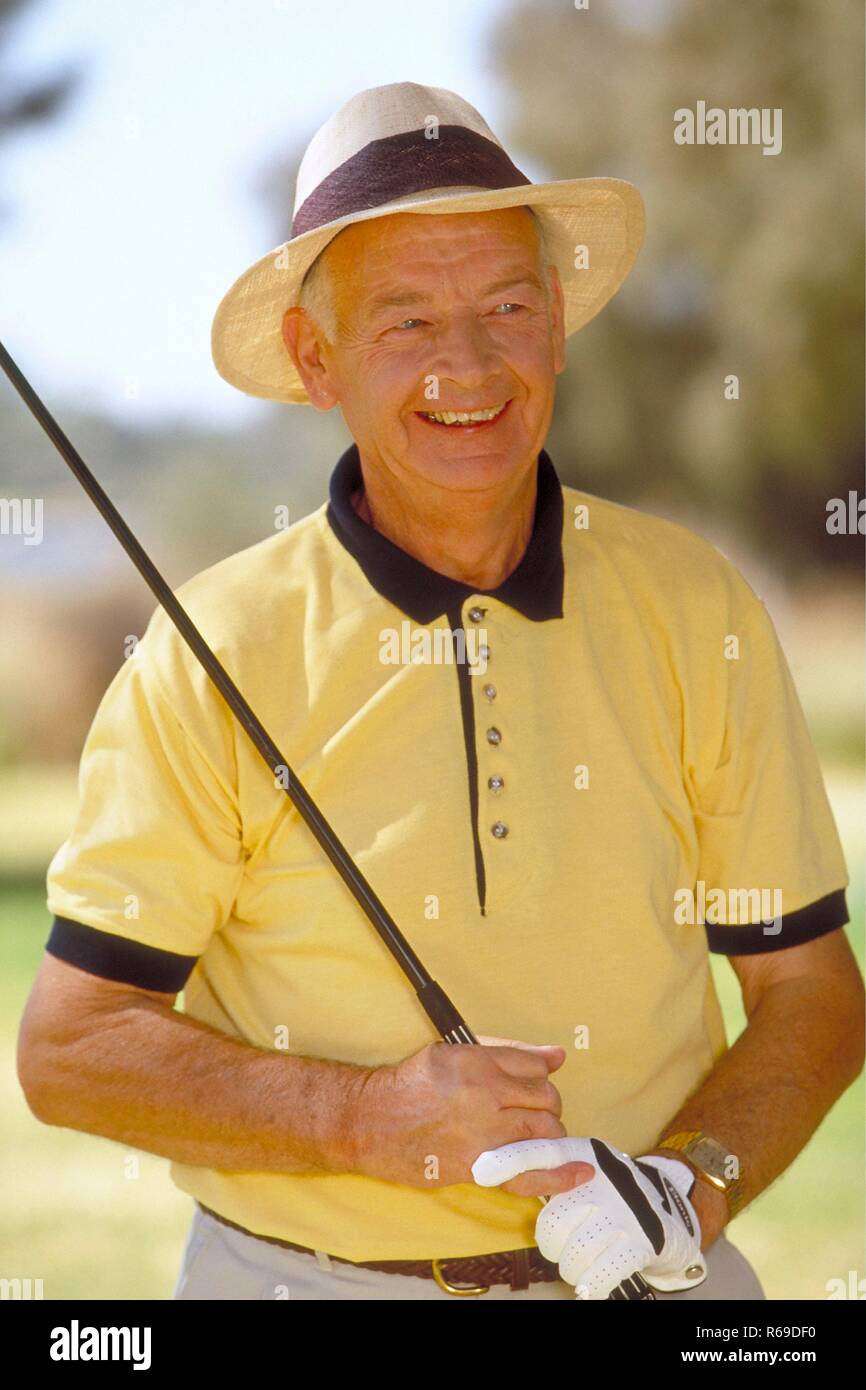 Outdoor, Portrait, Halbfigur, Mann Mitte 50, bekleidet mit gelbem Polohemd und weissem Hut mit seinem Golfschlaeger Stock Photo
