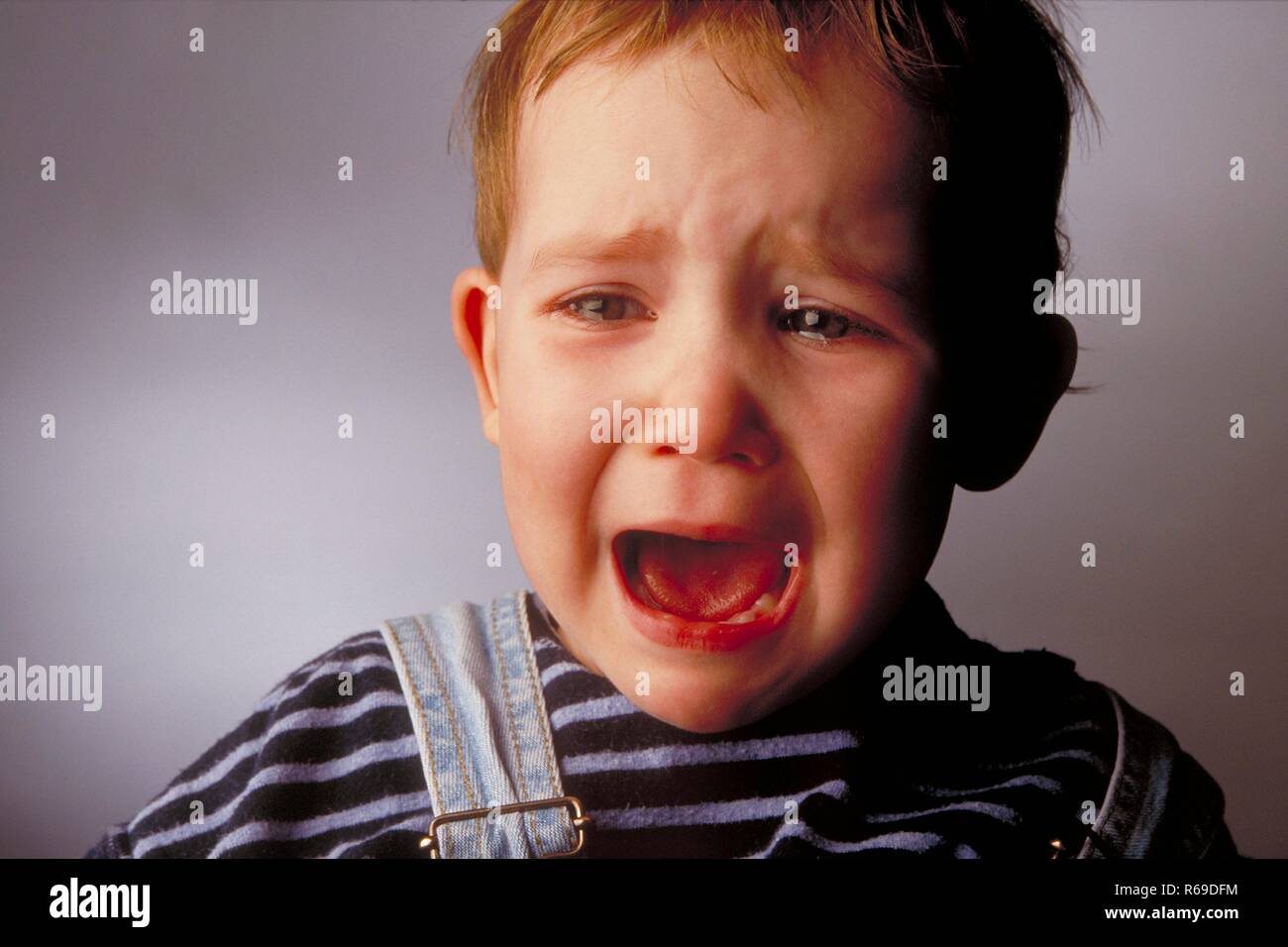 Portrait, Nahaufnahme, Innenraum, weinender 2-jaehriger rothaariger Junge  bekleidet mit gestreiftem T-Shirt Stock Photo