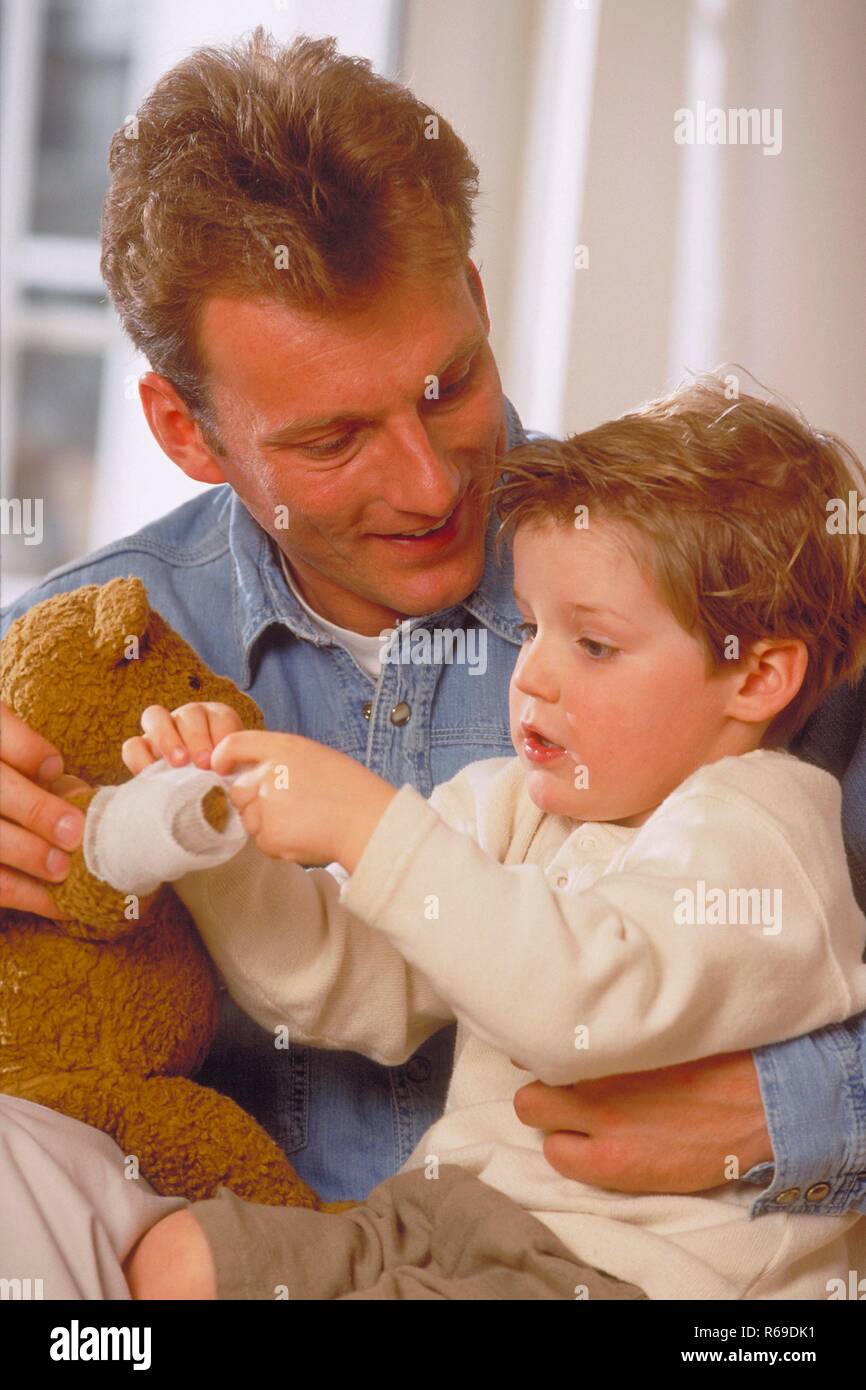 Portrait, Innenraum, Mann bekleidet mit Jeanshemd spielt  mit seinem 4-jaehrigen Sohn aund seinem Teddy Stock Photo
