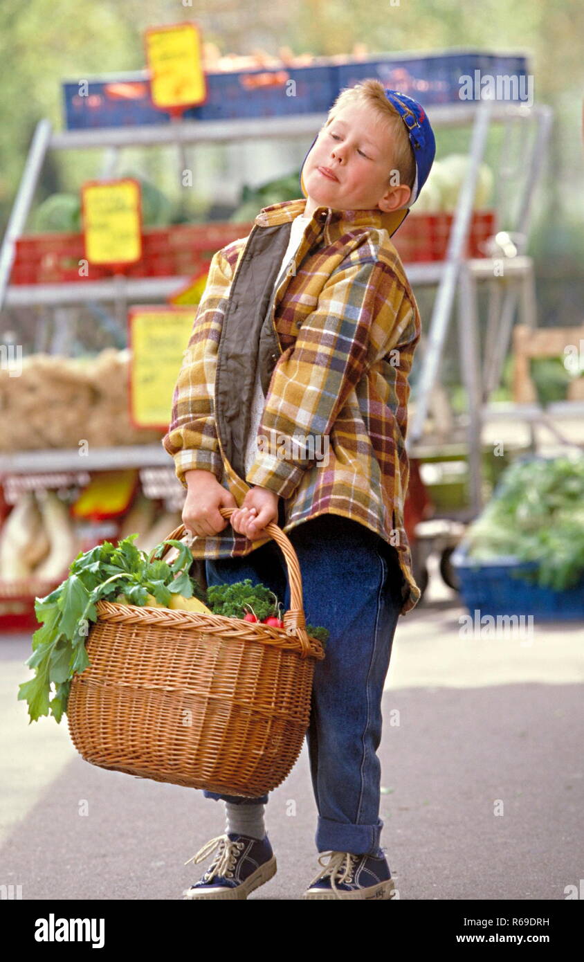 Portrait, Outdoor, Junge mit Baseballkappe schleppt einen schweren Einkaufskorb mit Gemuese und Obst vom Markt Stock Photo