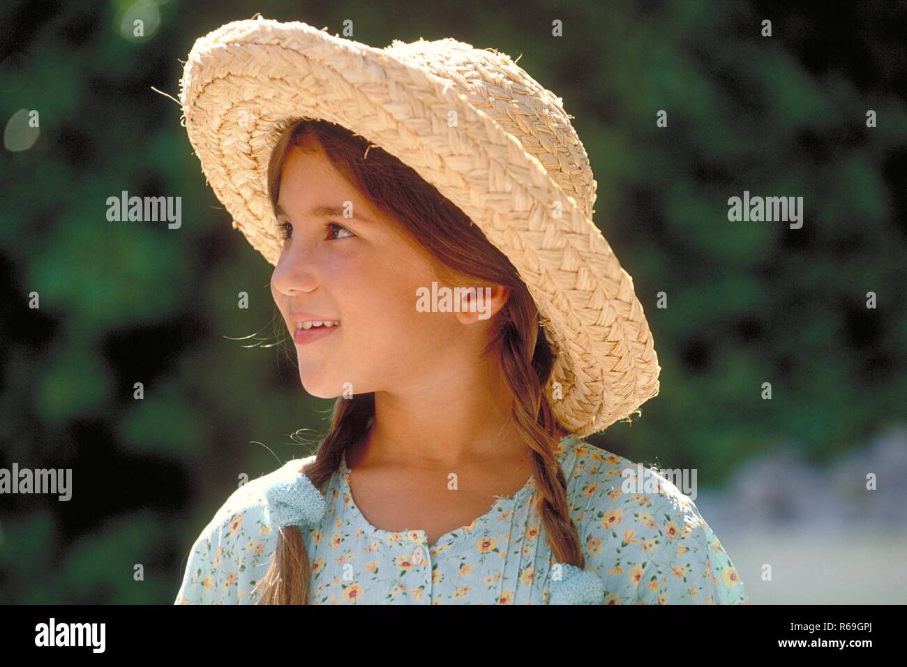 Portrait, Outdoor, Profil von Maedchen, 8 Jahre alt, mit braunen geflochtenen Zoepfen Haaren bekleidet mit hellblau gebluemten Kleid und Strohhut Stock Photo