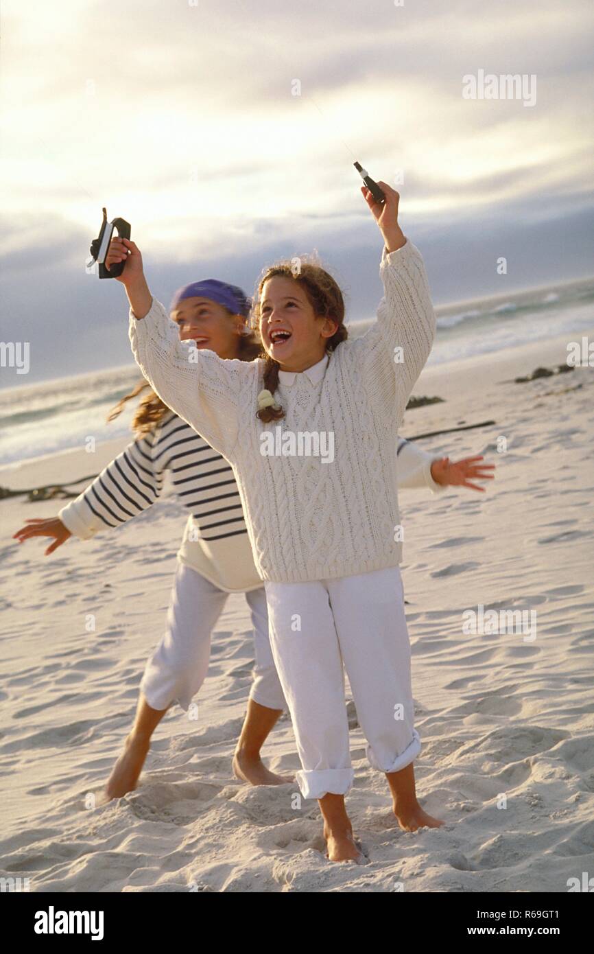 Strandszene, Ganzfigur, 2 barfuessige 8-10 Jahre Maedchen mit langen Haaren bekleidet mit hellen Pullovern und weissen Hosen lassen am Strand einen Drachen steigen Stock Photo