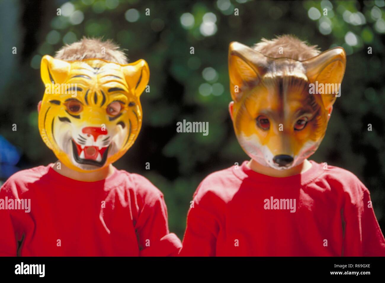 Portrait, Nahaufnahme, zwei 6 Jahre alte  Zwillings-Jungen mit kurzen blonden Haaren bekleidet mit roten T-Shirts, die ihre Gesichter hinter Tiermasken verbergen Stock Photo