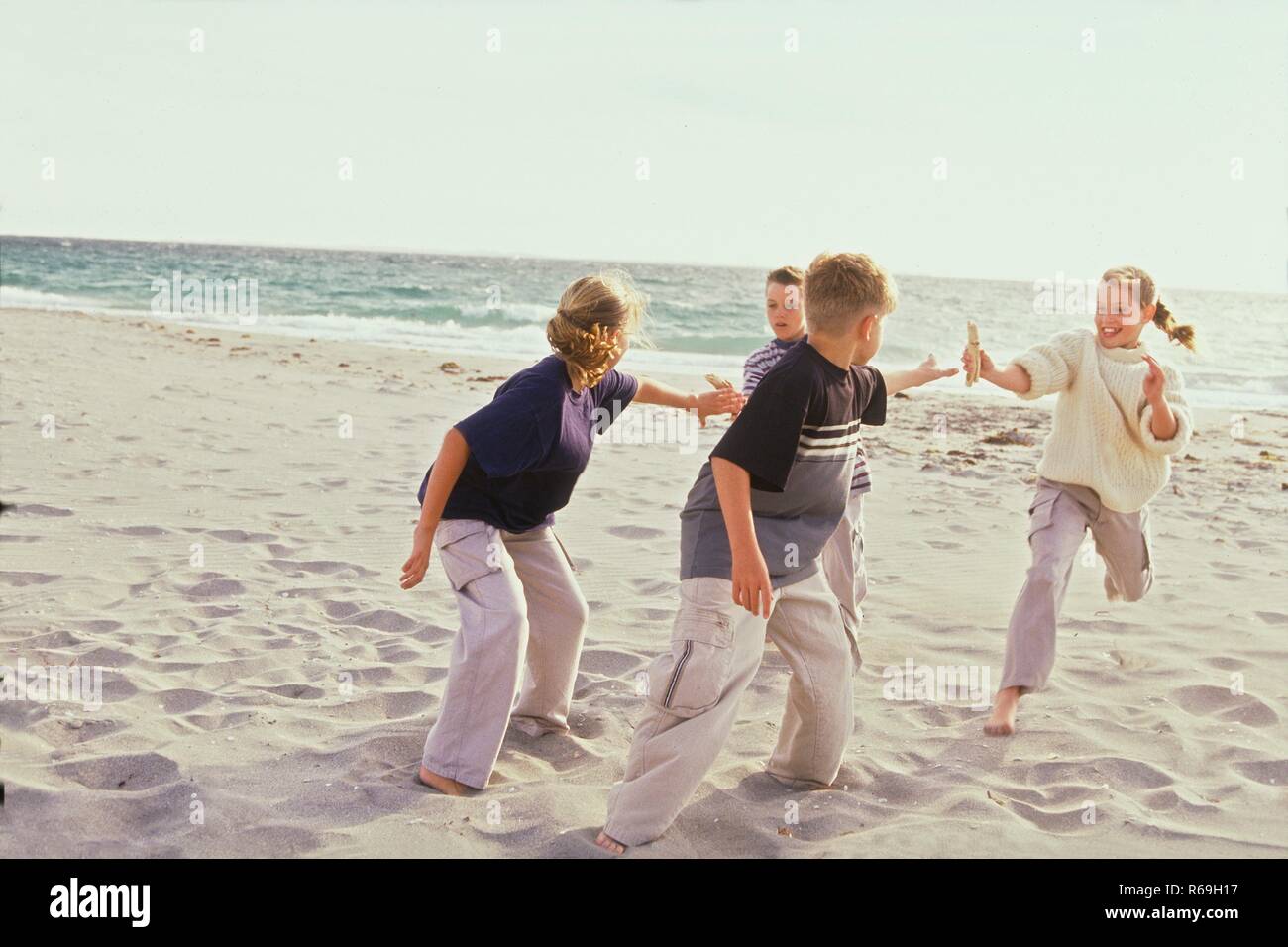 Strandszene, Portrait, 2 Maedchen und 2 Jungen im Alter von 10 -12 Jahren bei der Uebergabe des Stabes bei einem Staffellauf barfuss im Sand Stock Photo