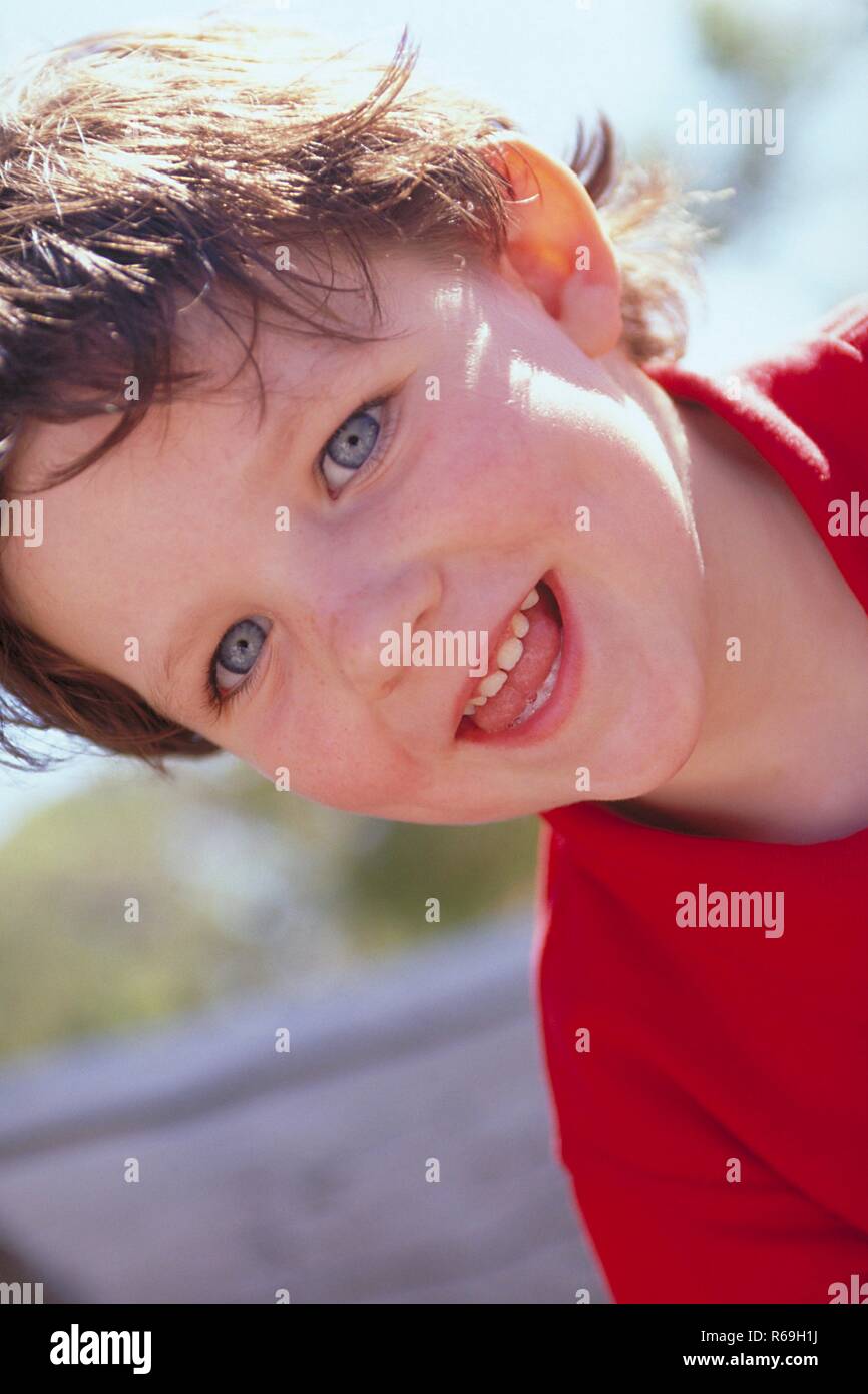 Outdoor, Portrait, lustiger 8-jaehriger Junge mit kurzen braunen Haaren und blauen Augen, bekleidet mit rotem Polohemd, zeigt lachend seine Zaehne Stock Photo