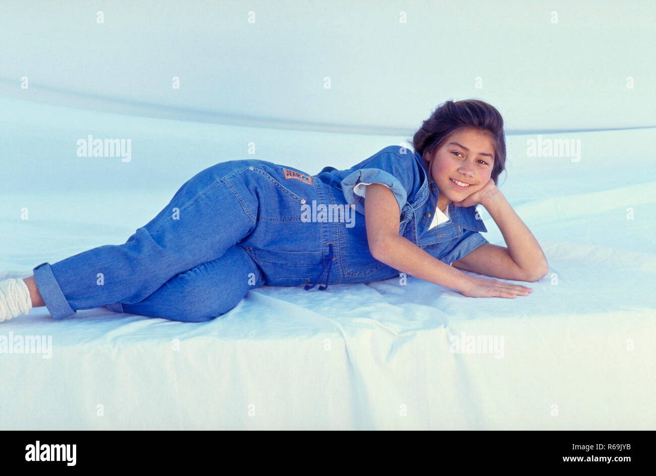 Portrait, laechelndes Maedchen indianischer Abstammung, 13 Jahre, mit langen schwarzen Haaren mit Jeans und Hemd und weissen Socken, liegt entspannt auf dem Boden Stock Photo