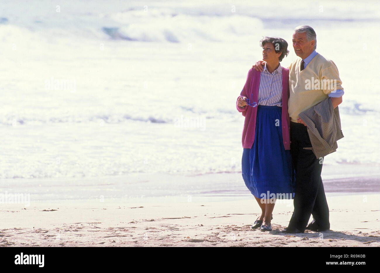 Portrait Seniorenpaar Mann Mit Schwarzer Hose Und Gelbem Pullover Und Frau Mit Blauem Rock Und Strickjacke Gehen Am Strand Spazieren Stock Photo Alamy