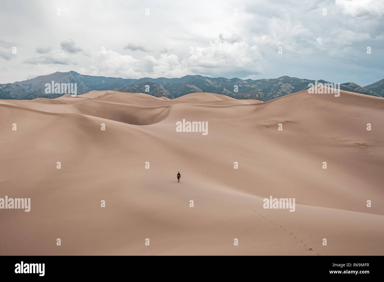 A man walking the giant sand dunes during stormy weather at Great Sand Dunes National Park in Colorado, USA Stock Photo