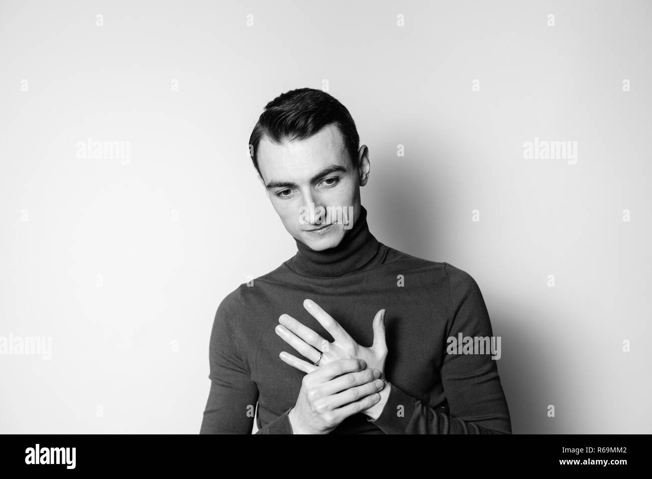 Close up black and white portrait of a young man wearing turtleneck jumper, looking to the side, against plain studio background Stock Photo