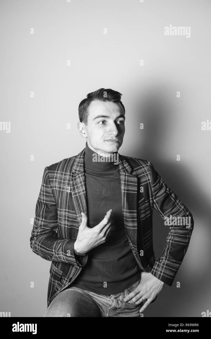 Close up black and white portrait of a young man wearing turtleneck jumper and the jacket, looking to the side, against plain studio background Stock Photo