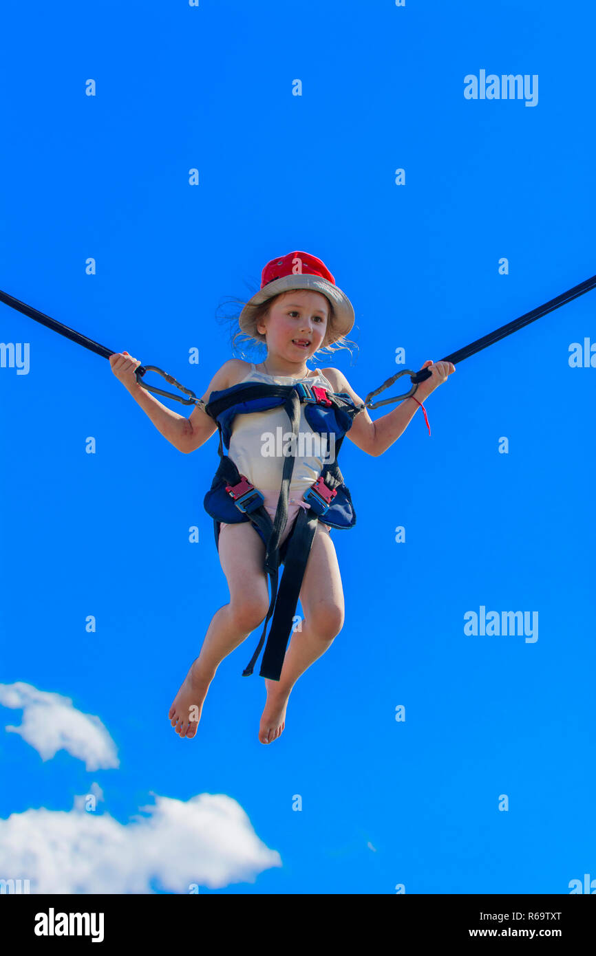 Children jumping on a trampoline with rubber ropes against the blue sky