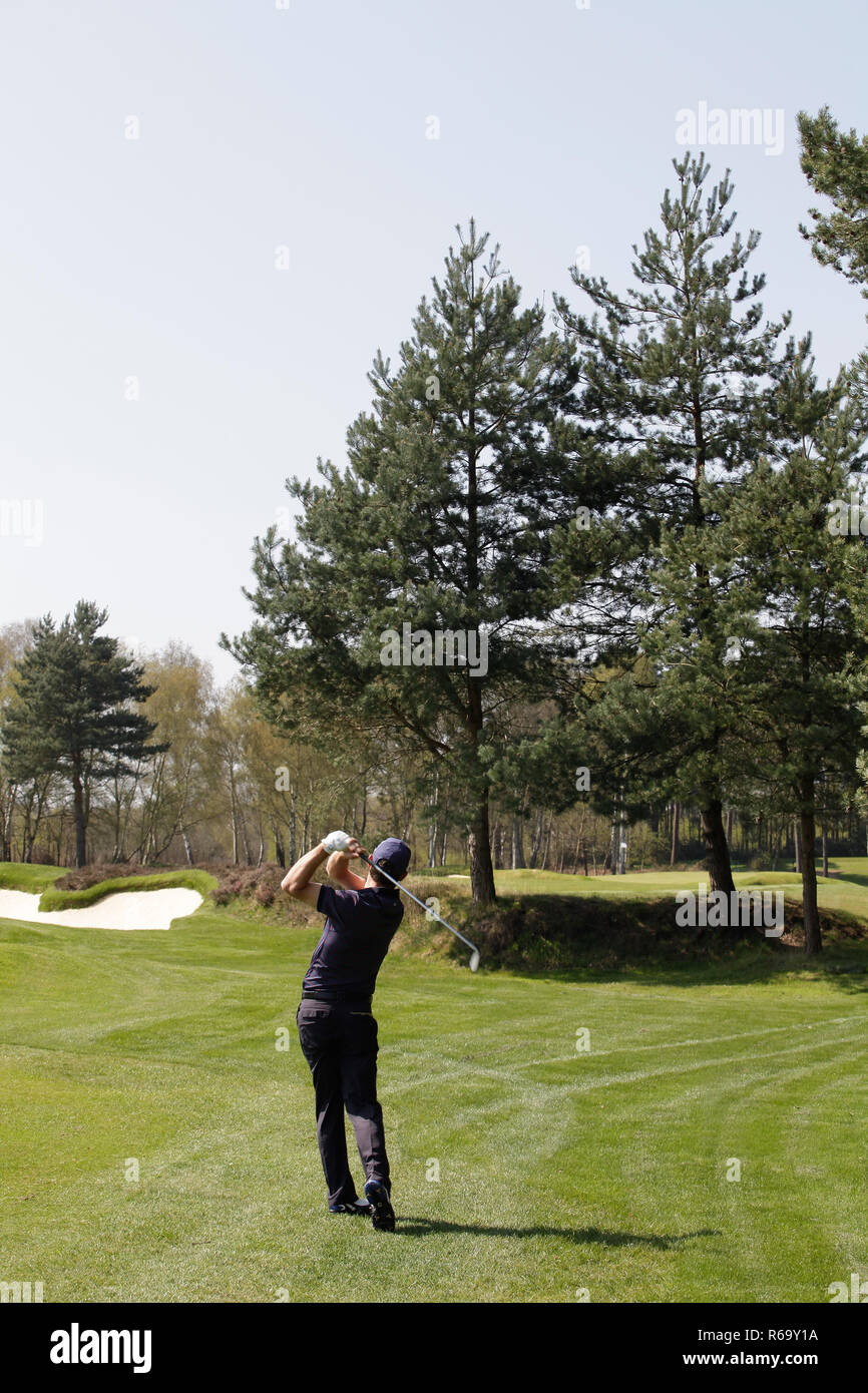 Golfer playing a skilful approach shot over trees to a distant green Stock Photo