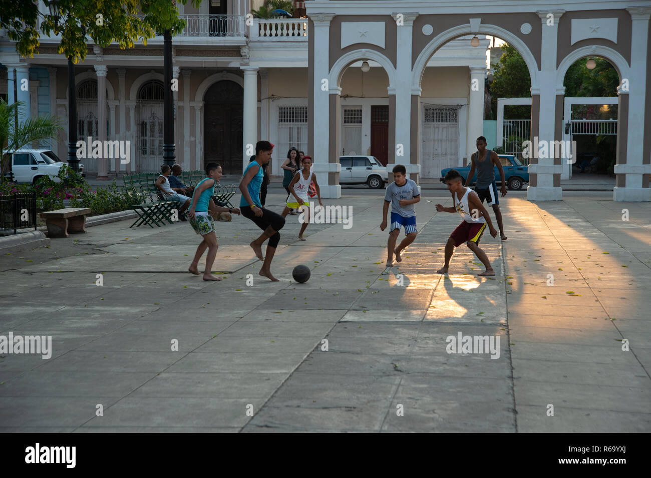 Cuban boys playing football in the main square of Cienfuegos Cuba as the sun begins to set casting a golden glow on the street Stock Photo