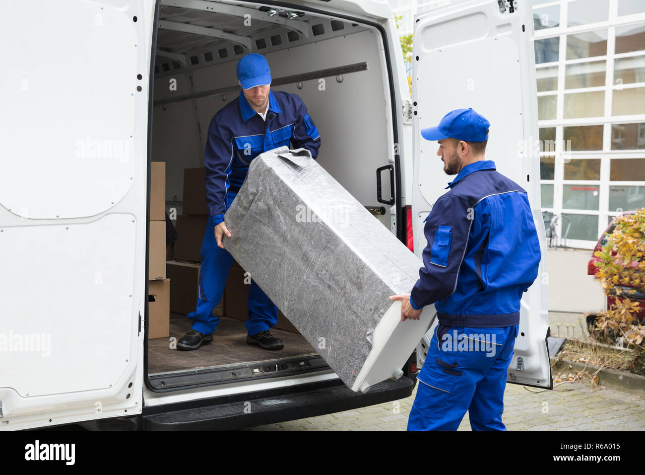 Two Delivery Men Unloading Furniture From Vehicle Stock Photo