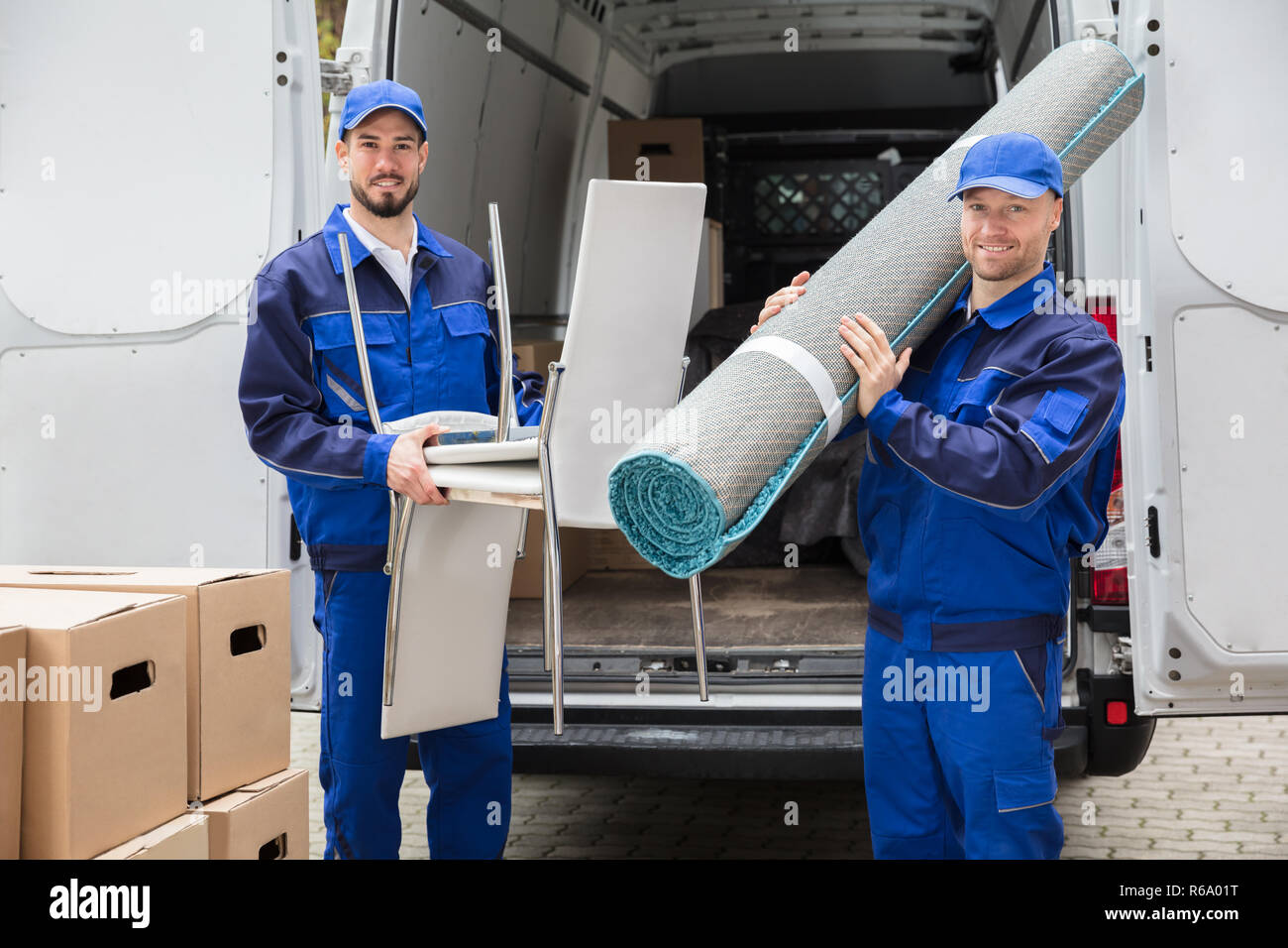 Two Delivery Men Holding Chairs And Carpet Stock Photo