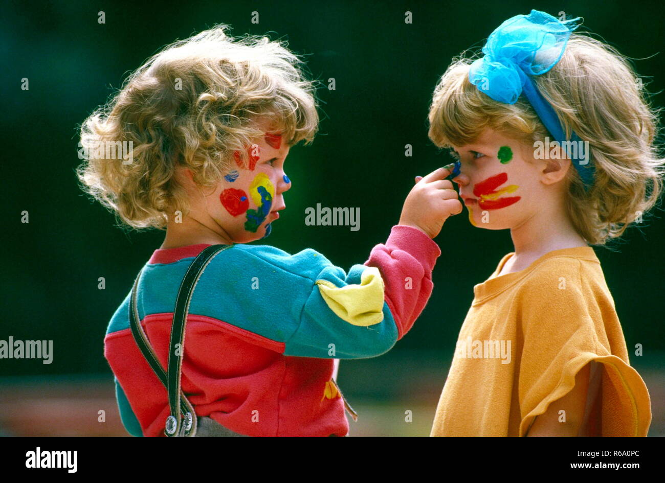Portrait, 2 blondgelockte Kinder, Junge und Maedchen, 4 Jahre, bemalen sich gegenseitig ihre Gesichter mit Fingerfarben Stock Photo