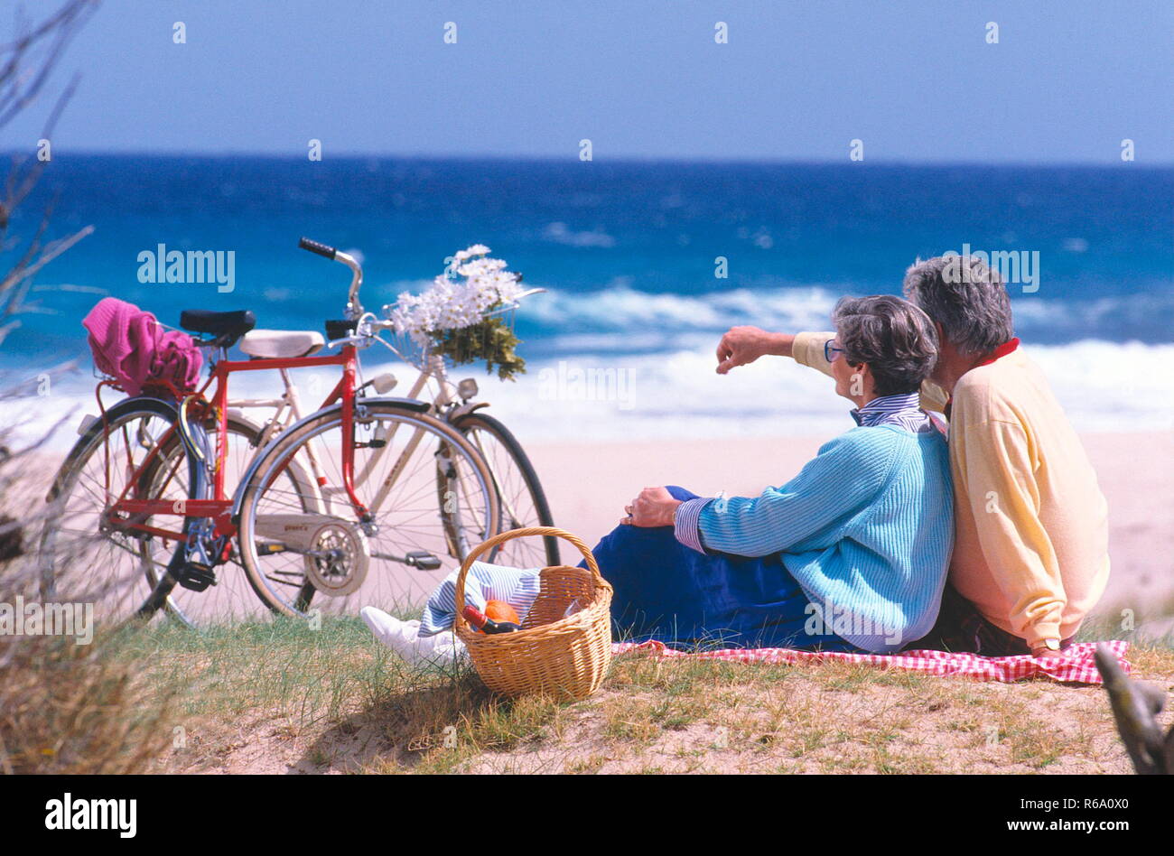 Strandszene, Seniorenpaar mit Fahrraedern sitzt am Strand Stock Photo
