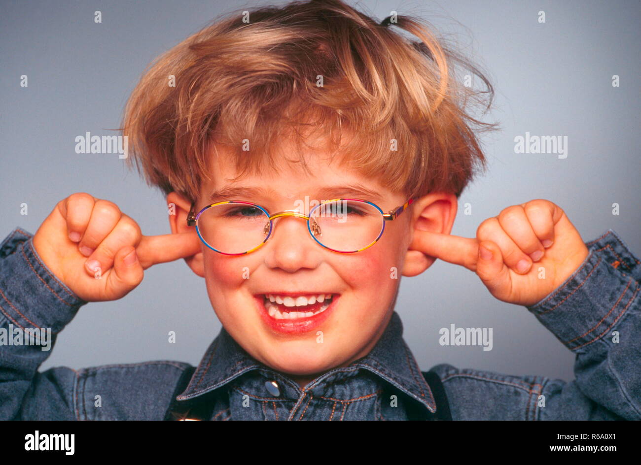 Portrait, Close-up, lachender Junge mit Brille, 6 Jahre, haelt sich die Ohren mit den Zeigefingern zu Stock Photo